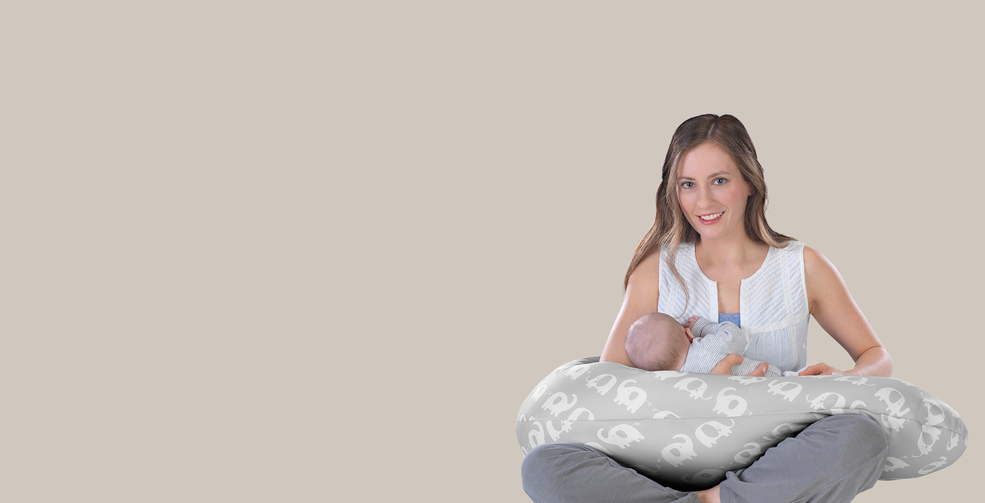 Eine Frau hält ein Baby auf einem stillenden Kissen mit Elefantenmuster, lächelnd und sitzend in entspannter Haltung vor einem beigen Hintergrund. Markenhinweis: Theraline.