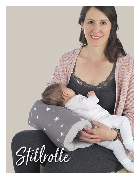 Eine Frau hält ein Baby, das auf einem grauen Kissen mit weißen Sternen liegt. Der Kontext ist ein neutraler, heller Hintergrund. Text: \